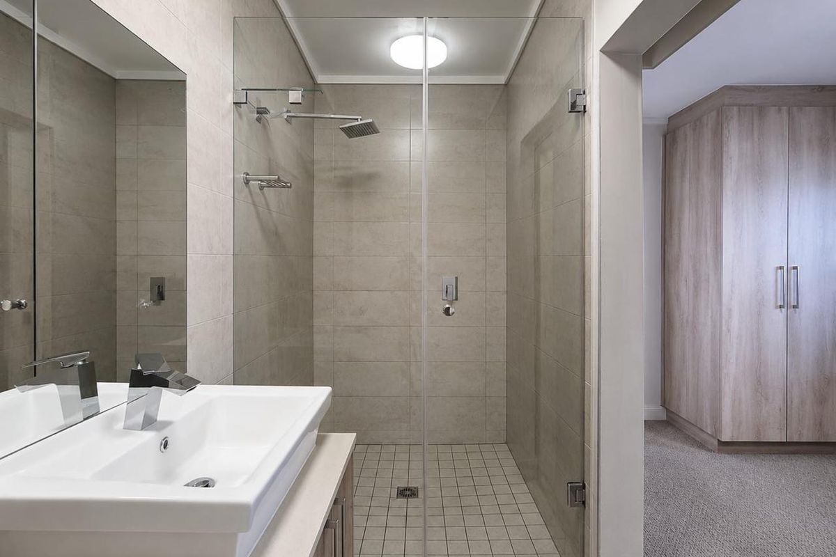 Modern bathroom featuring a frameless glass shower, rain shower head, wall-mounted basin with vanity, and adjacent built-in wardrobe storage.