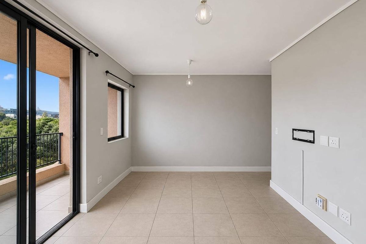 A bright, empty living area featuring neutral tiled flooring, modern pendant lighting, and a sliding glass door leading to a private balcony.