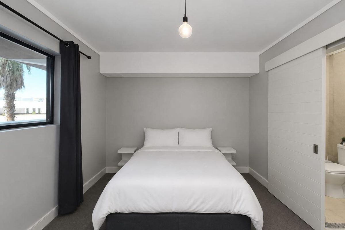 A modern bedroom featuring neutral grey walls, carpeted flooring, a pendant light, and a sliding door providing access to an en-suite bathroom.