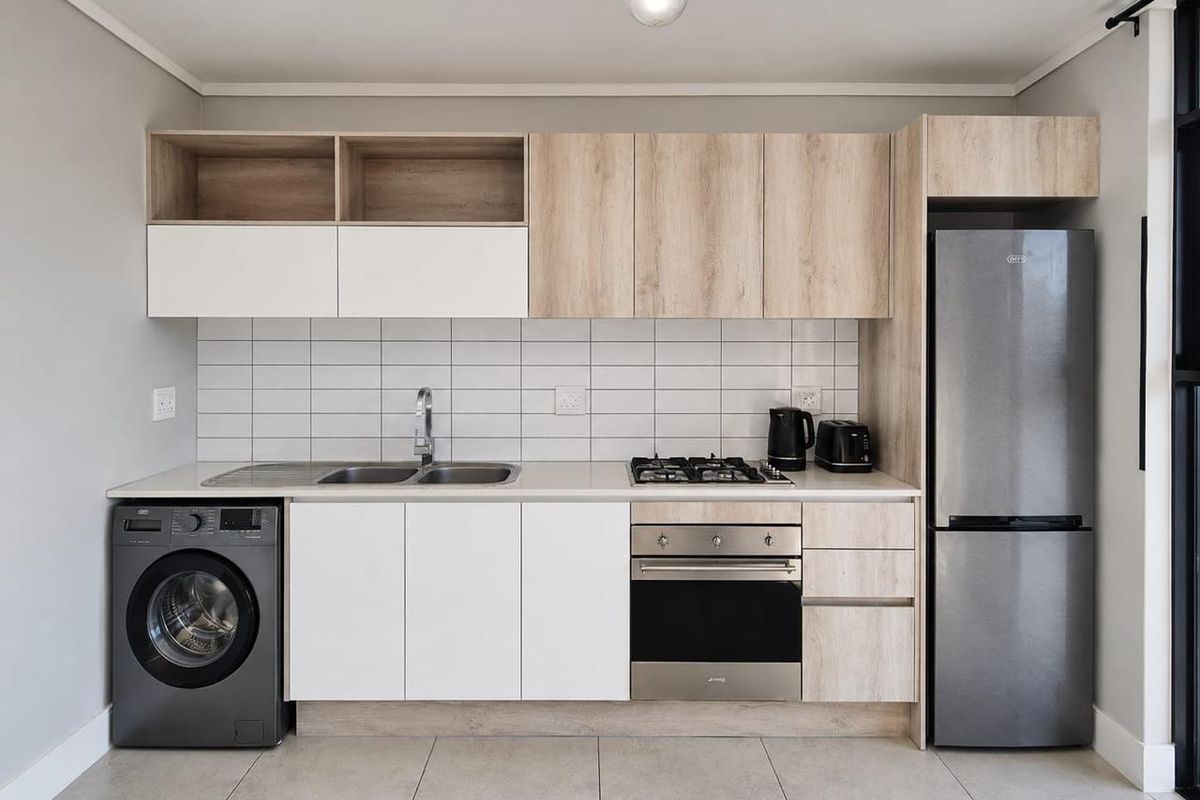 Modern kitchen featuring light wood-tone and white cabinetry, tiled backsplash, gas hob, built-in oven, and integrated space for a washing machine.