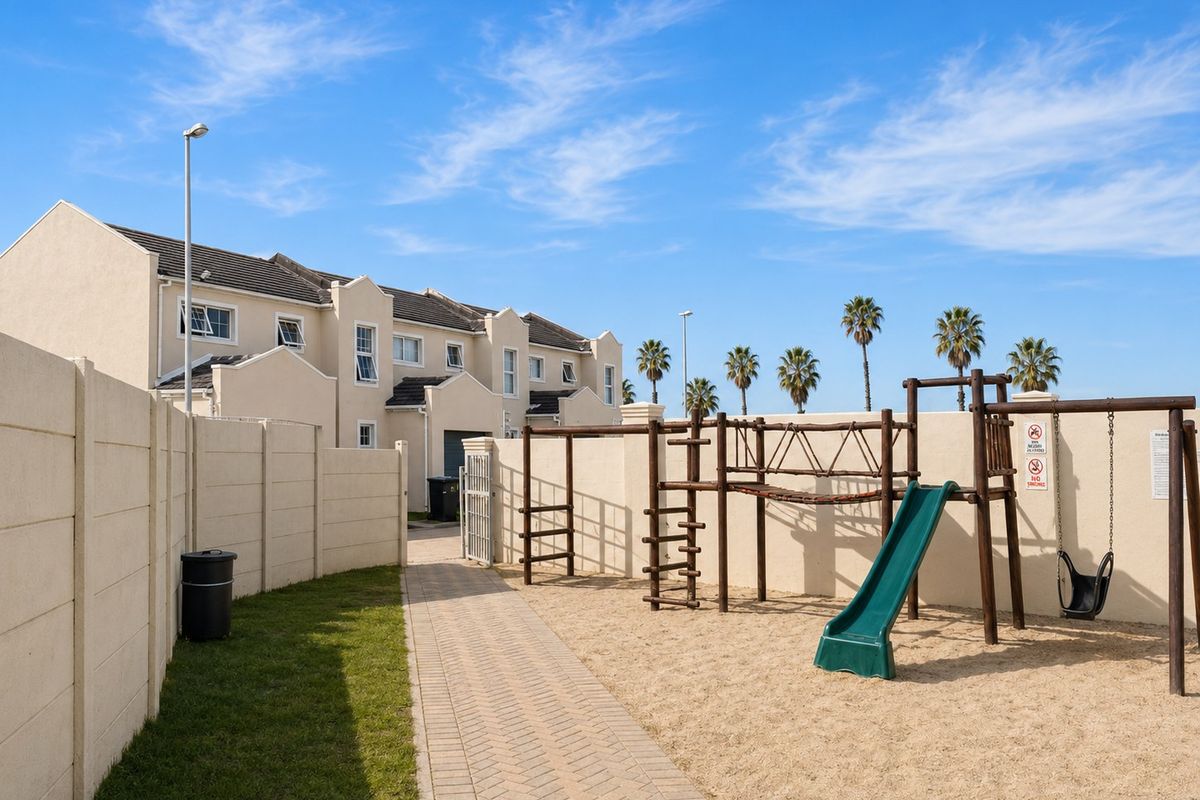 A well-maintained communal outdoor area featuring a paved walkway, sand-based playground with climbing frame and swing set, enclosed by precast concrete boundary walls.