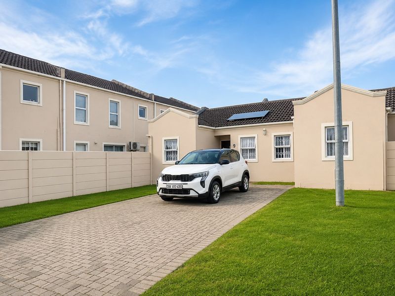Front elevation of the apartment featuring a paved driveway, well-maintained lawn, solar water heater, and secure boundary walling.