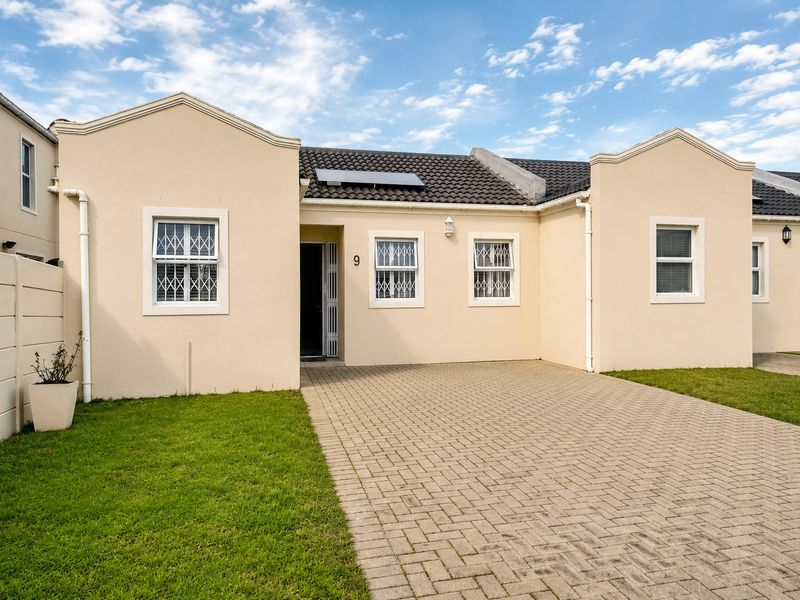 Front elevation of a well-maintained apartment featuring a paved driveway, security bars on windows, and a solar water heating system on the roof.