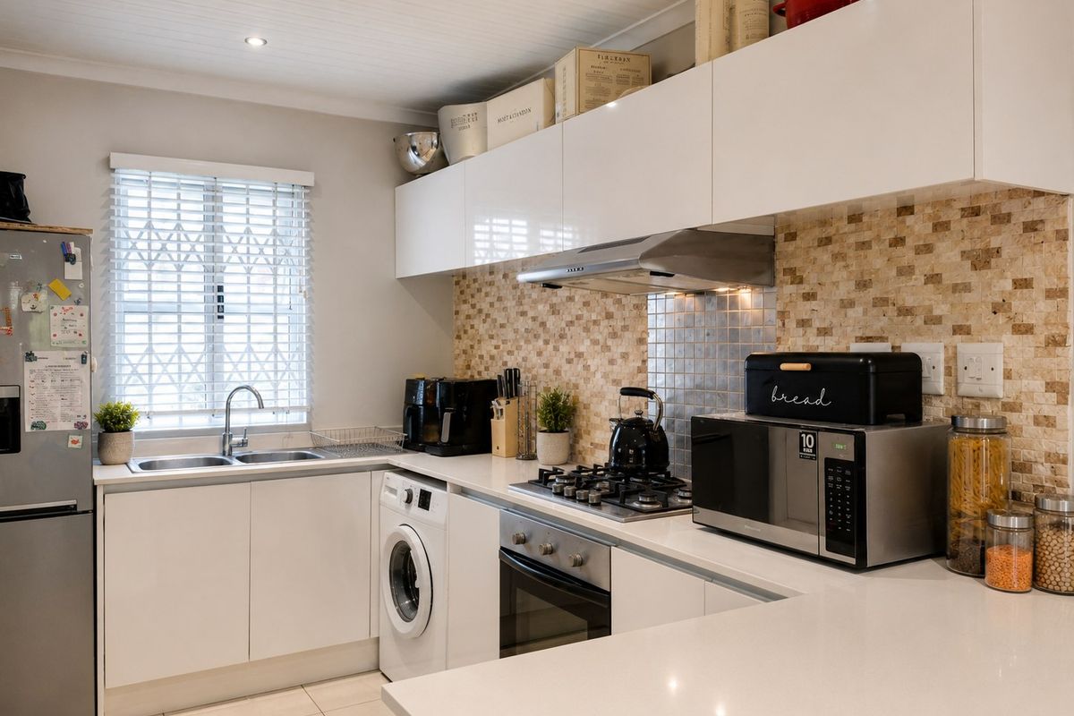Modern kitchen featuring white cabinetry, stone countertops, a gas hob, built-in oven, extractor fan, and a tiled backsplash with integrated laundry facilities.