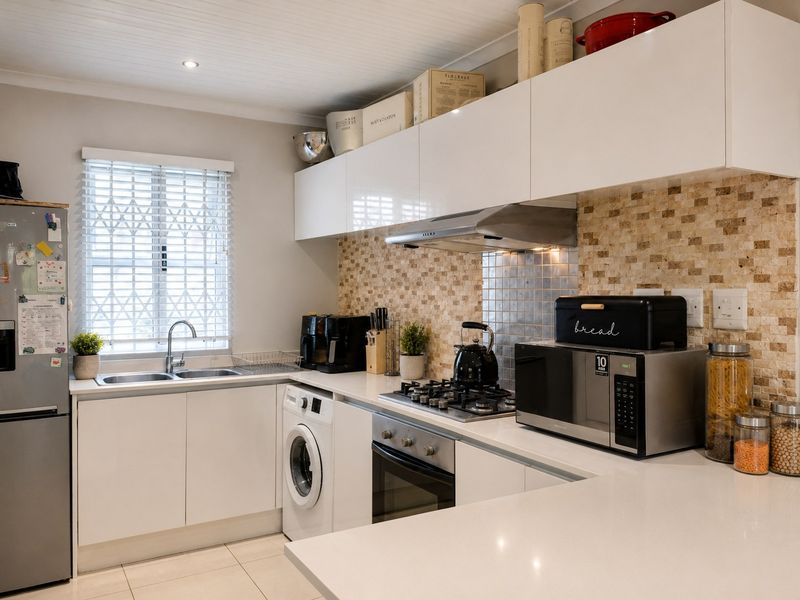 Modern kitchen featuring white cabinetry, stone countertops, a gas hob, built-in oven, extractor fan, and a tiled backsplash with integrated laundry facilities.