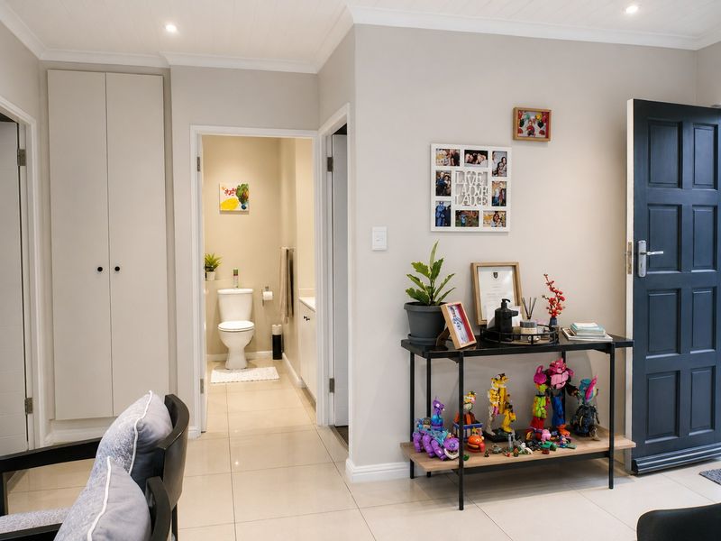 A well-maintained hallway featuring tiled flooring, recessed downlights, and a built-in storage cupboard, providing access to an adjacent bathroom.