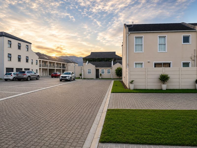 A well-maintained apartment complex exterior featuring paved parking areas, neat lawns, and modern multi-story residential buildings at sunset.