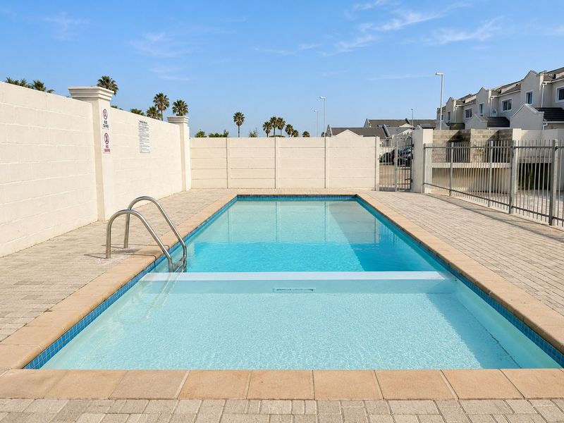 A well-maintained communal swimming pool area featuring paved surrounds, boundary walls, and secure metal fencing within an apartment complex.