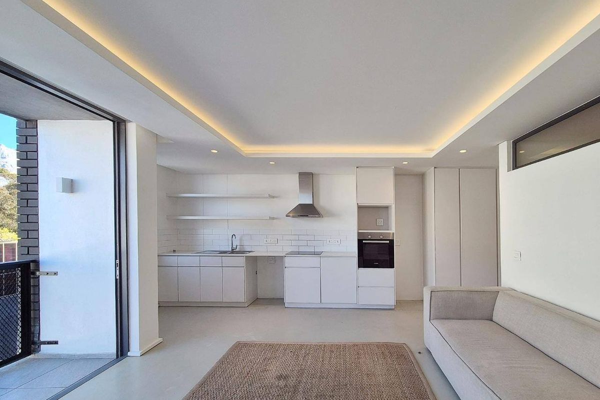 Modern open-plan living area featuring a sleek kitchen with built-in appliances, recessed ceiling lighting, and seamless access to a private balcony.