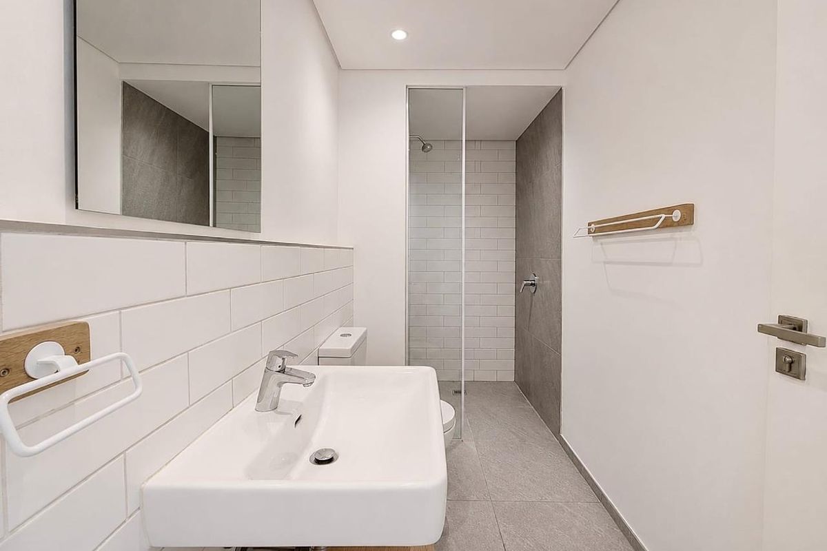Modern, minimalist bathroom featuring a wall-mounted basin, walk-in shower with glass screen, and neutral subway and large-format tiling.
