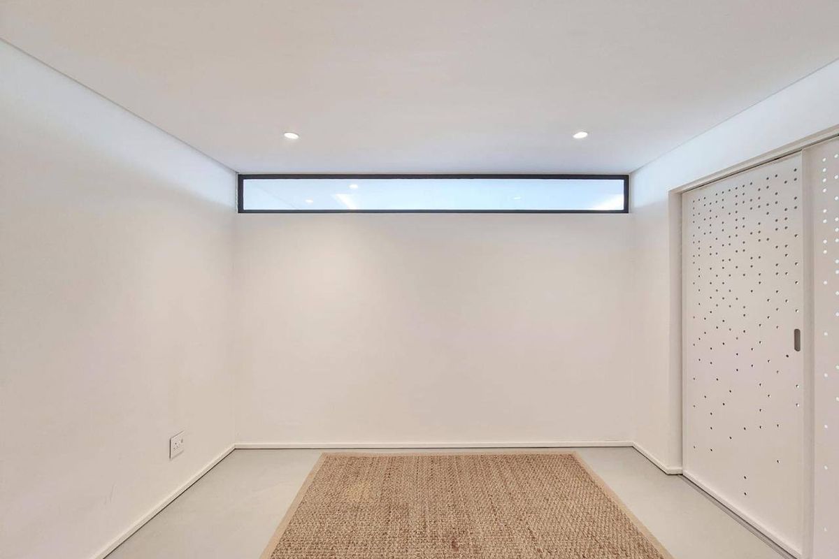 A bright, minimalist bedroom featuring a high-level clerestory window, recessed lighting, and a modern built-in wardrobe with decorative perforated doors.