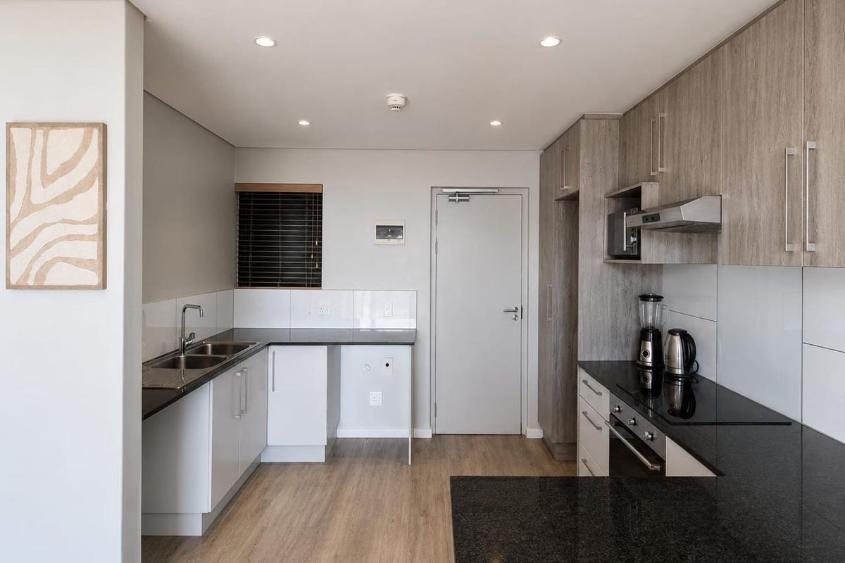 Modern kitchen featuring granite countertops, built-in oven, electric hob, extractor fan, and ample cabinetry with a clean, contemporary finish.