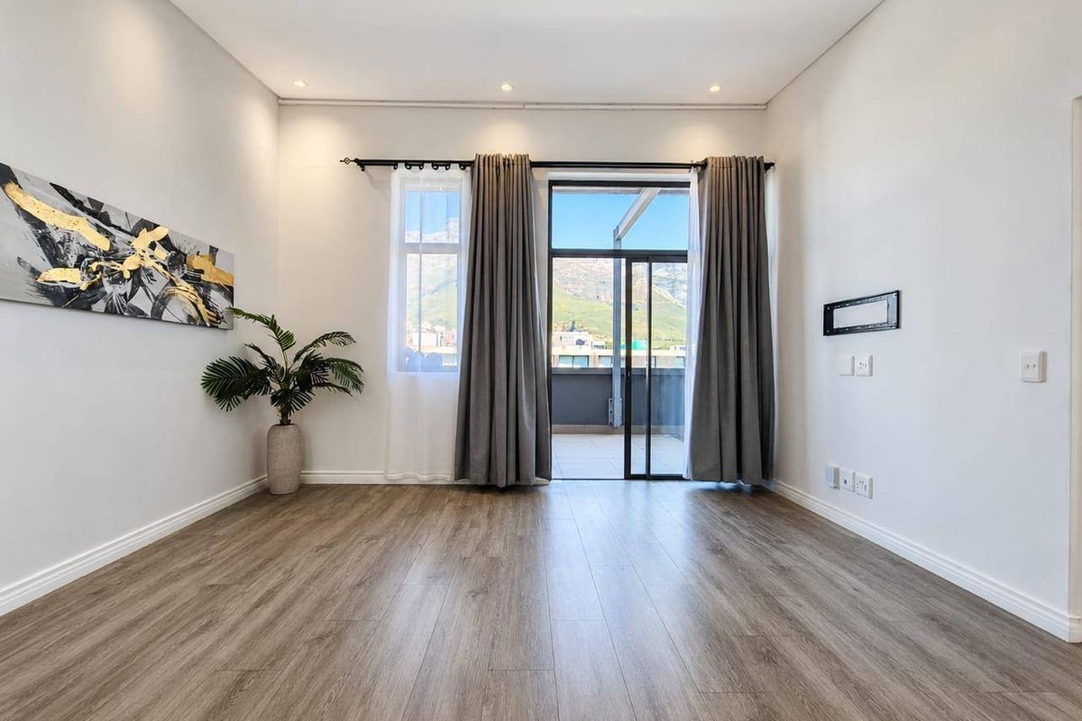 A bright, empty living room featuring modern laminate flooring, recessed lighting, and a sliding glass door providing access to an outdoor balcony.