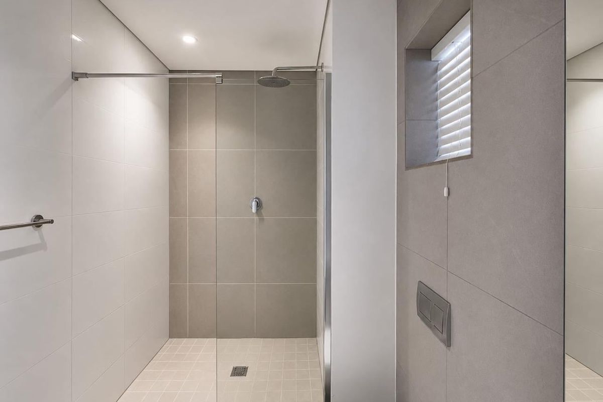 Modern bathroom featuring a spacious walk-in shower with a rain shower head, glass screen, and neutral floor-to-ceiling tiling.