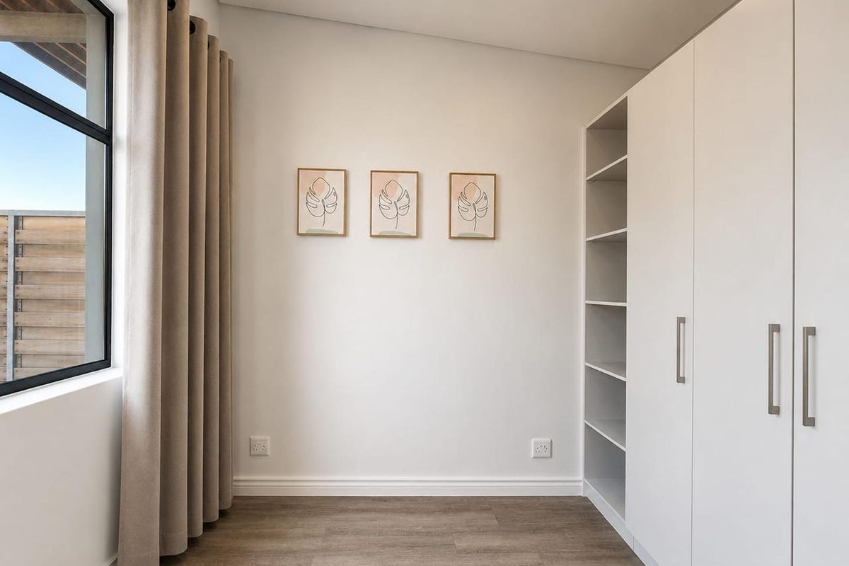 A bright, modern bedroom featuring neutral walls, laminate flooring, and a spacious built-in wardrobe with integrated shelving.