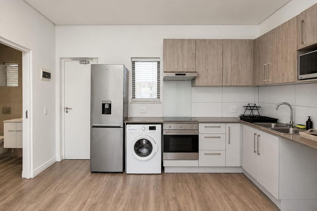 Modern kitchen featuring light wood-tone cabinetry, integrated appliances, stainless steel oven and hob, and durable laminate flooring with a clean, contemporary finish.