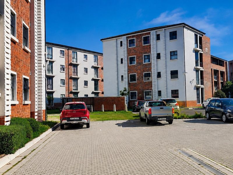 Exterior view of a multi-story apartment complex featuring brick and plaster facades with a paved parking area.