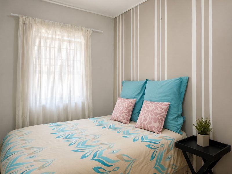 A cozy bedroom featuring a neutral striped accent wall and natural light through a window with fitted curtain rails.