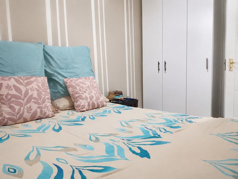 A well-maintained bedroom featuring a neutral striped accent wall and a clean, white built-in wardrobe.