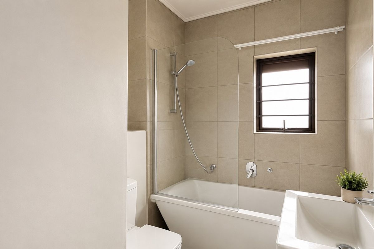 Modern bathroom featuring a bathtub with a glass shower screen, tiled walls, and a contemporary basin with chrome fixtures.