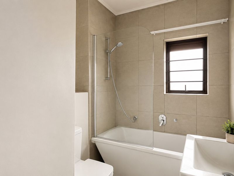 Modern bathroom featuring a bathtub with a glass shower screen, tiled walls, and a contemporary basin with chrome fixtures.