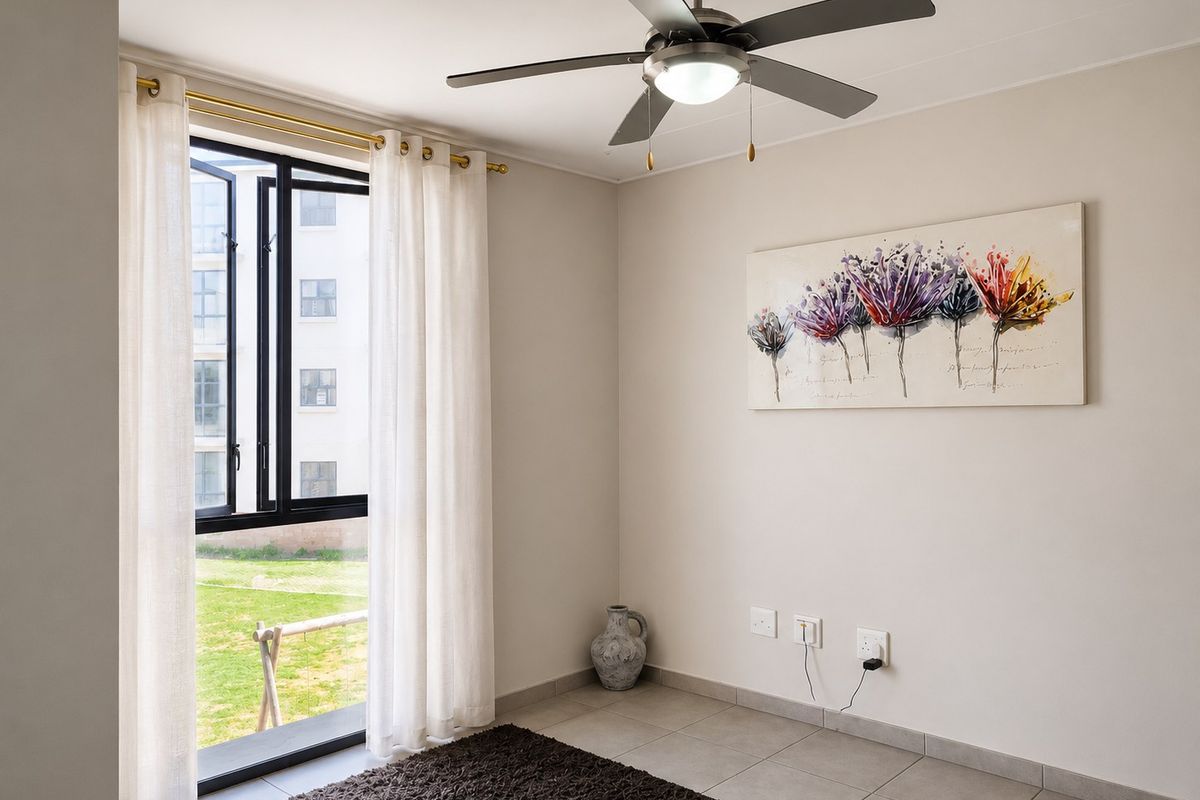 A bright and neutral bedroom featuring tiled flooring, a modern ceiling fan, and large windows overlooking the complex grounds.