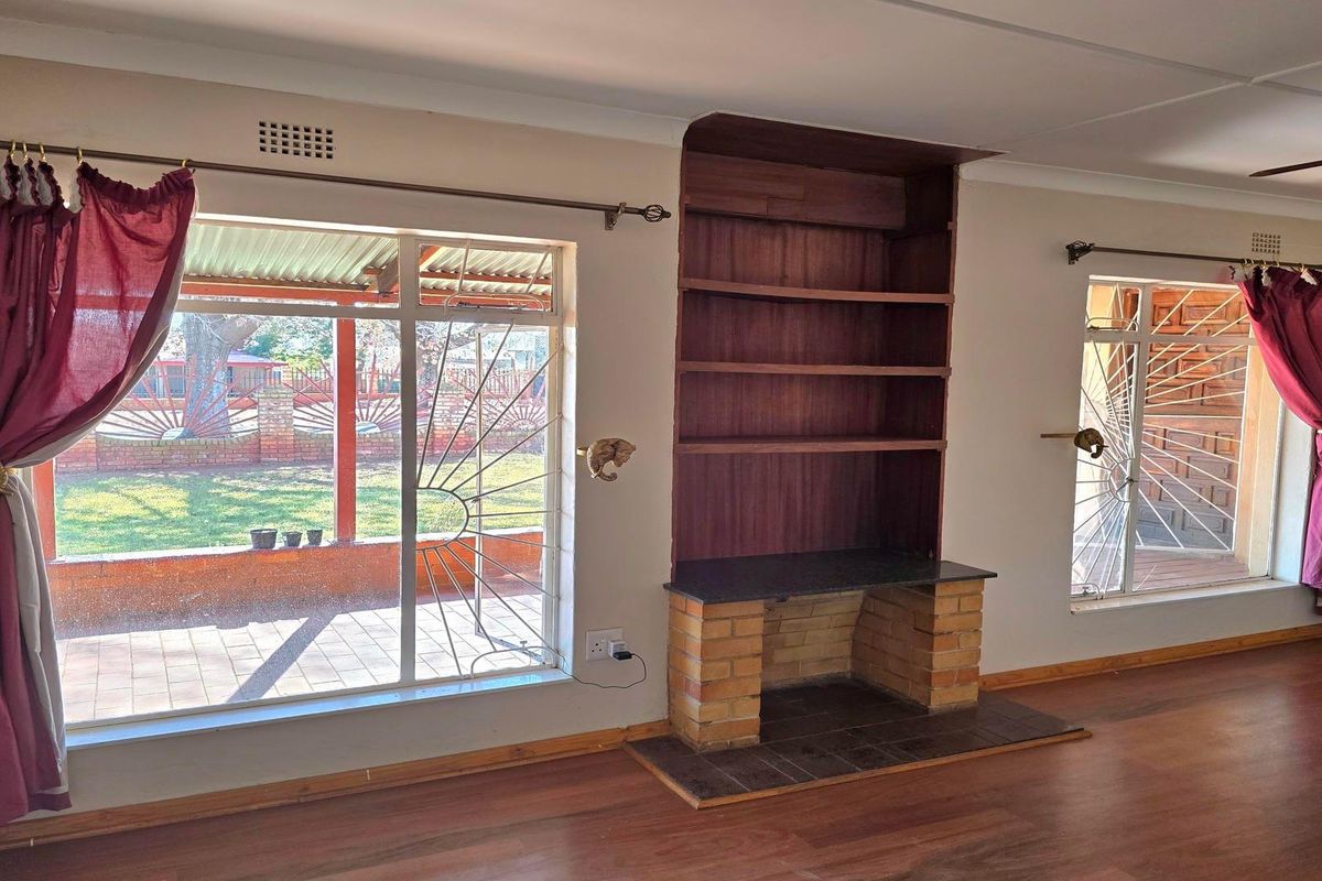 Spacious living area featuring a built-in fireplace with integrated shelving, laminate flooring, and large windows with security bars overlooking the rear patio.