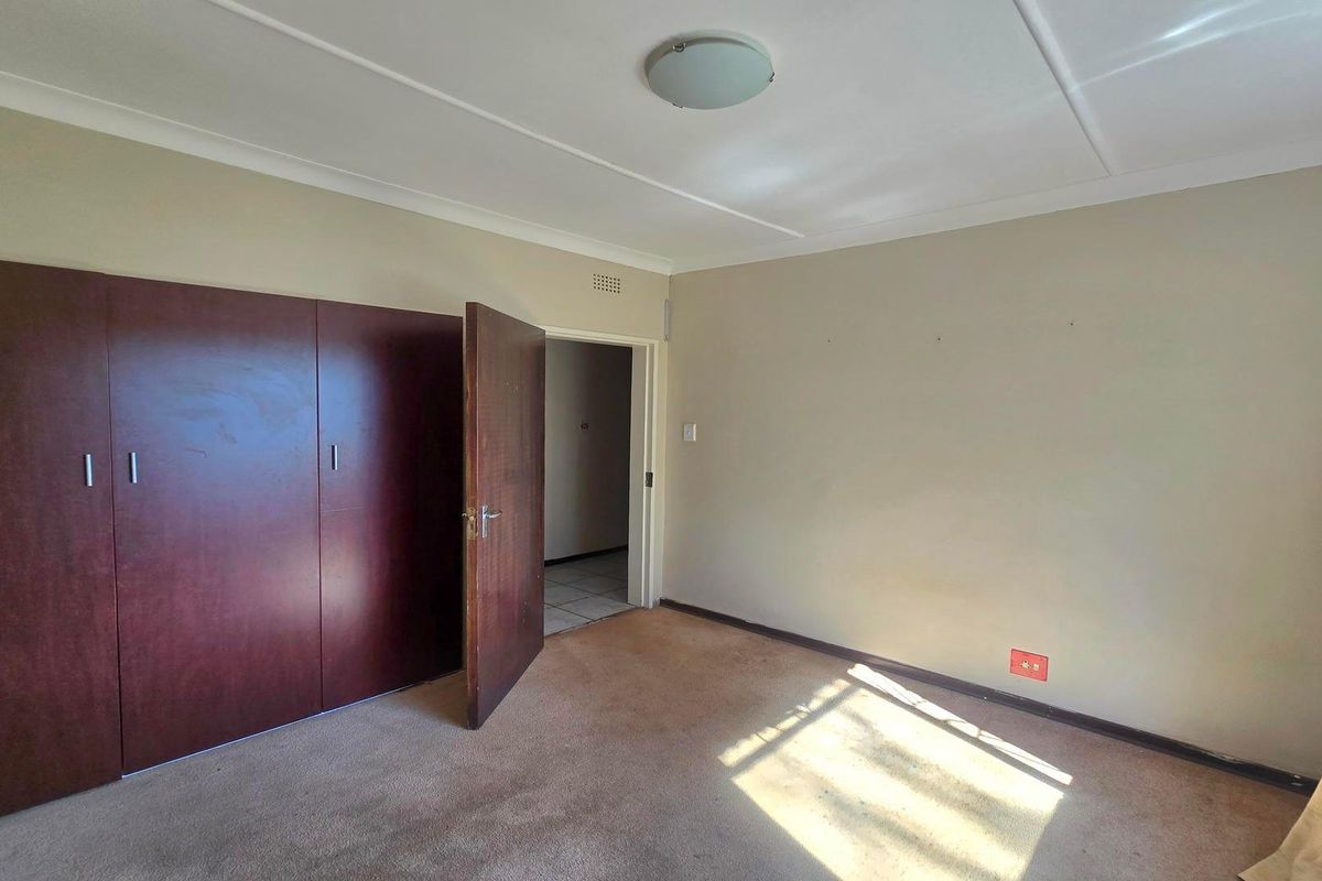 An empty bedroom featuring built-in wooden cupboards, carpeted flooring, and neutral wall finishes, offering a blank canvas for personalization.