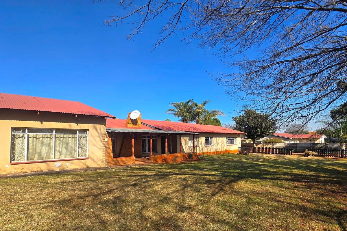Rear view of a single-story house featuring a corrugated metal roof, covered patio area, and a spacious backyard with perimeter fencing.