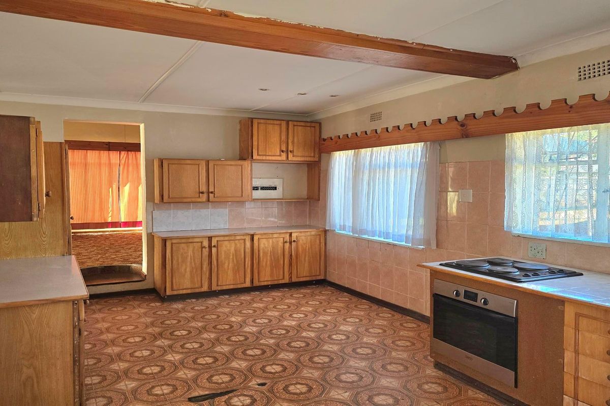A spacious, dated kitchen featuring original wooden cabinetry, built-in oven and hob, tiled splashbacks, and patterned flooring, offering significant potential for modern renovation.