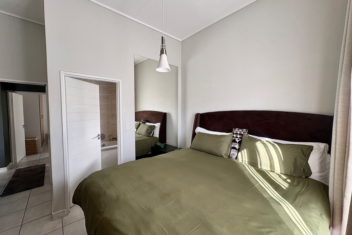 A well-maintained bedroom featuring tiled flooring, a modern pendant light, a full-length wall mirror, and direct access to an en-suite bathroom.