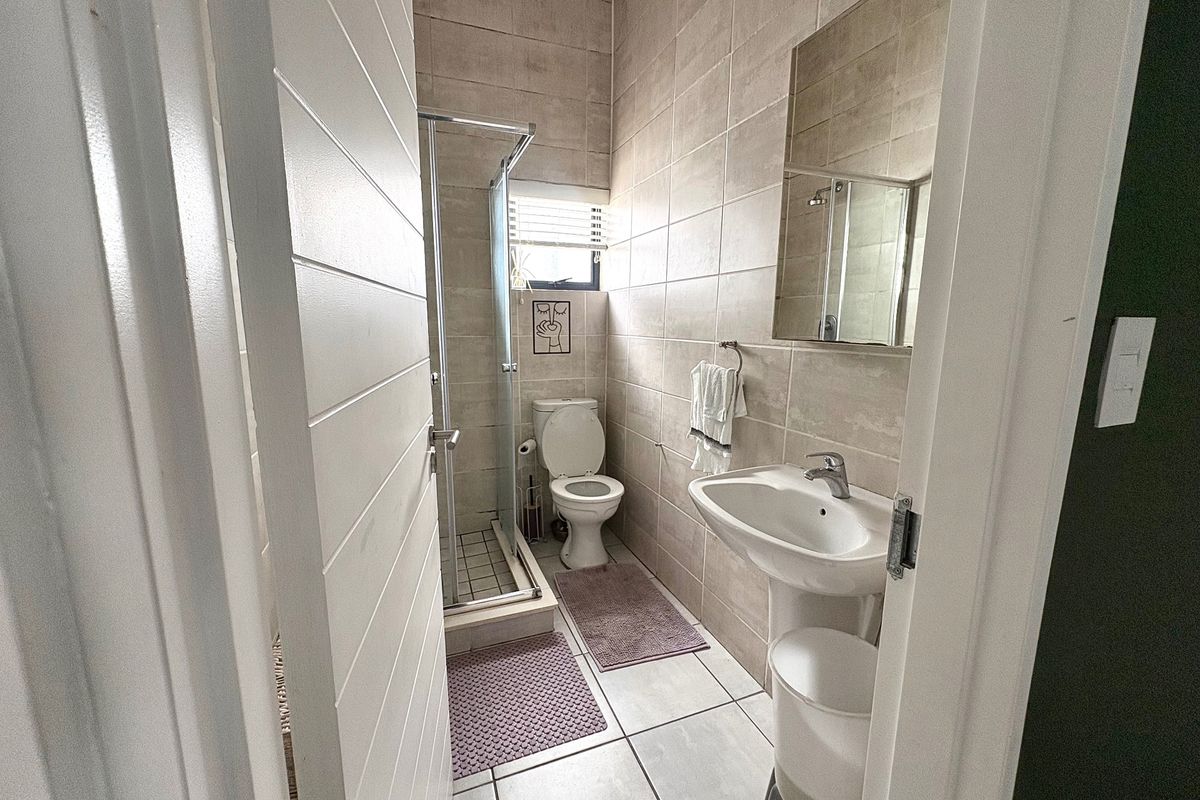 A compact bathroom featuring a pedestal basin, a glass-enclosed shower, and a toilet, finished with neutral wall and floor tiles.