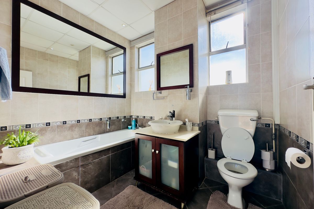 A well-maintained bathroom featuring a built-in bathtub, a vanity with a vessel sink, a toilet, and neutral-toned wall and floor tiling.