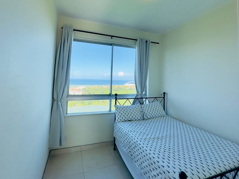 A bright bedroom featuring tiled flooring and a large window offering expansive coastal and landscape views.