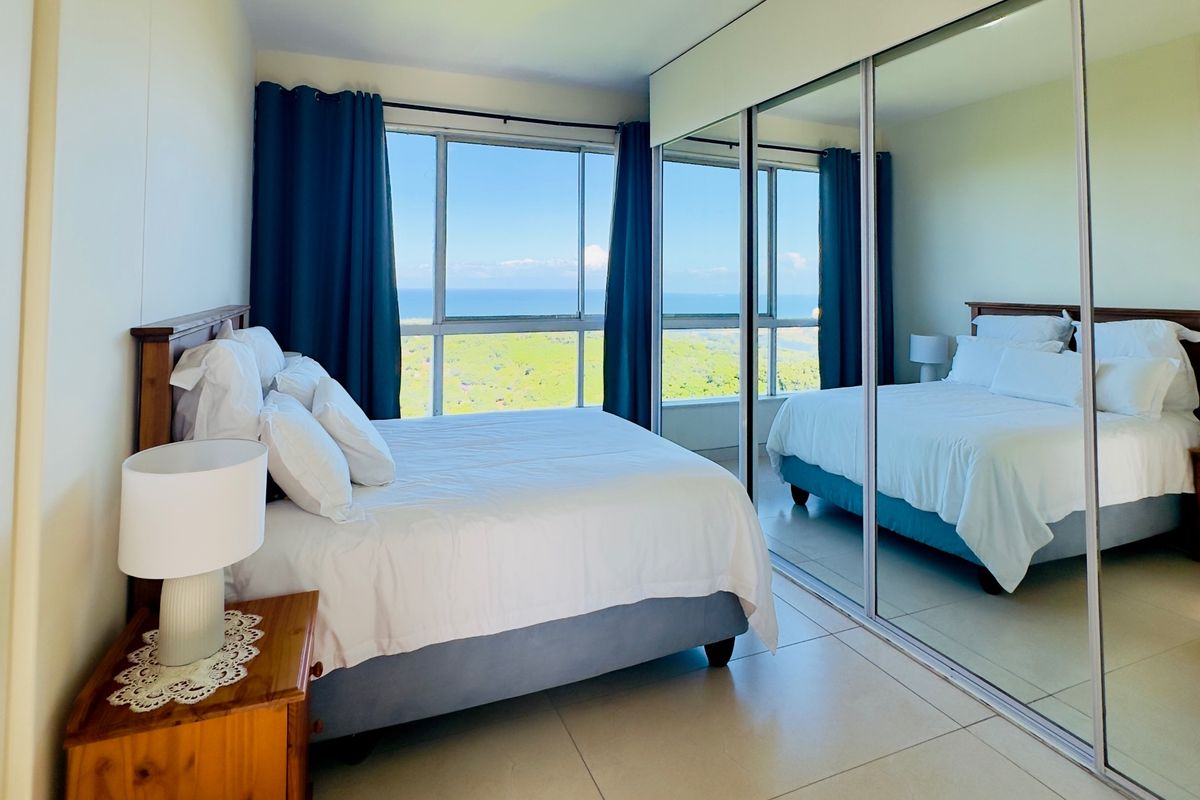 A bright bedroom featuring large windows with scenic views, tiled flooring, and a spacious built-in mirrored wardrobe.