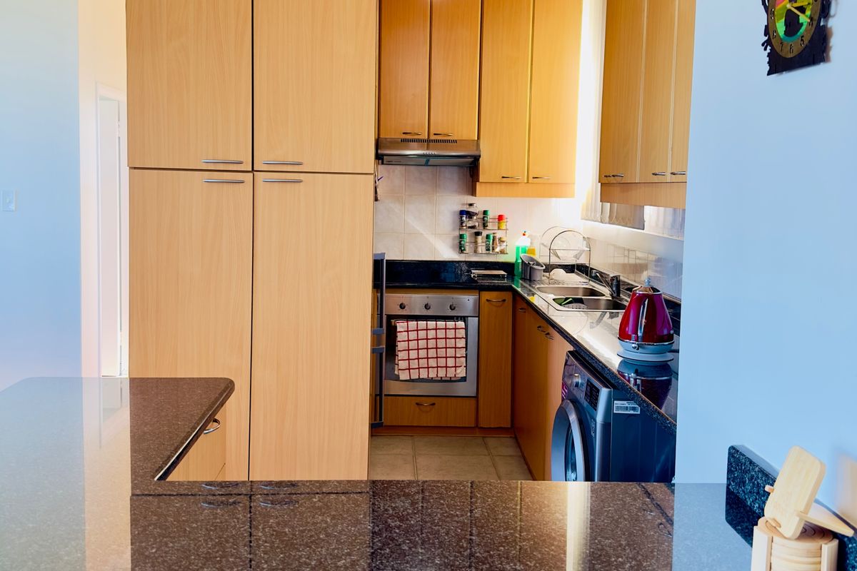 A compact kitchen featuring light wood cabinetry, dark granite countertops, integrated oven, and a tiled backsplash with efficient layout.