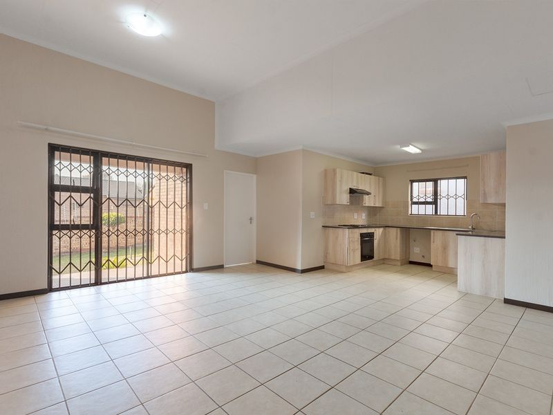 Spacious open-plan living and kitchen area featuring neutral tiled flooring, light wood-finish cabinetry, and direct access to the rear garden via a sliding door.