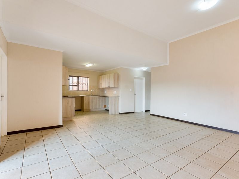 Spacious open-plan living area featuring neutral tiled flooring and a functional kitchen with built-in cabinetry and laminate countertops.