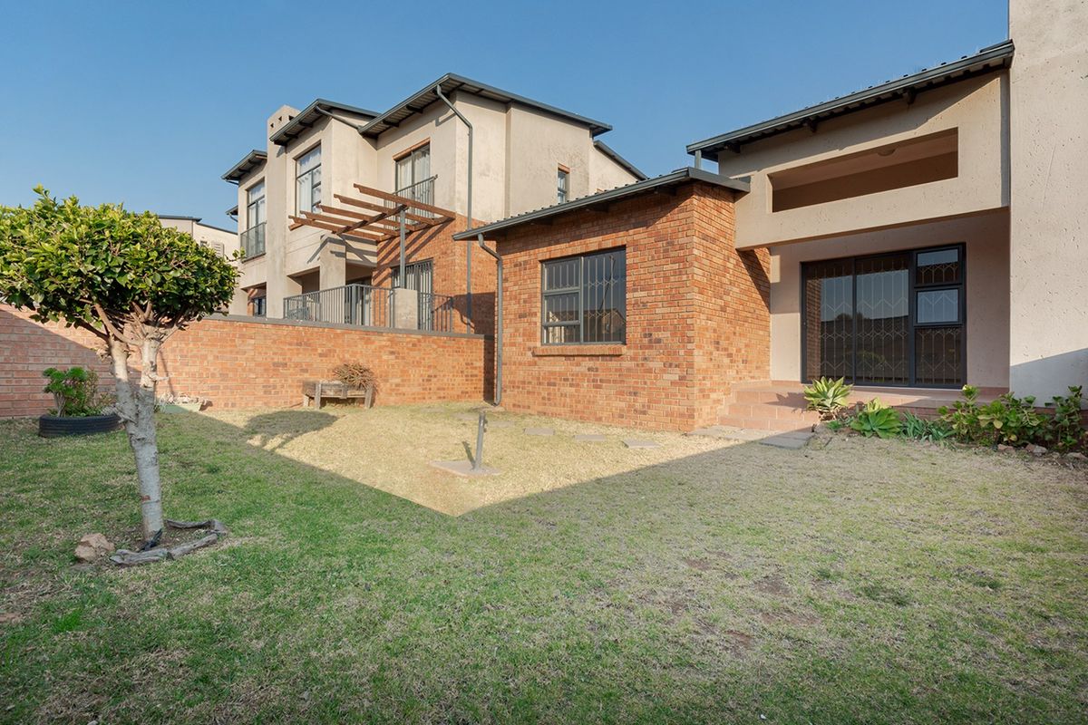 Rear view of the townhouse featuring a private garden, brick facade, and a covered patio area with sliding glass doors.