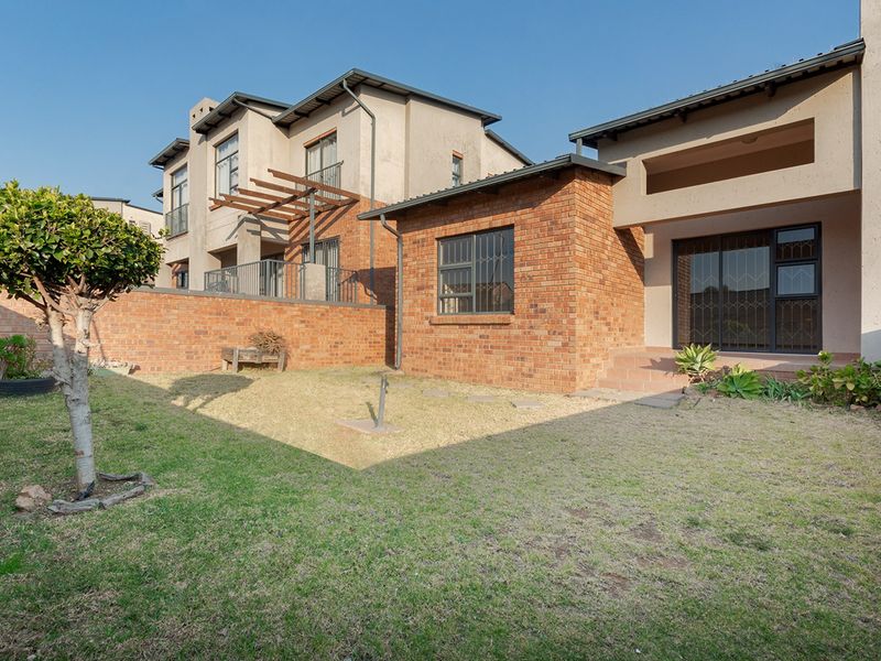 Rear view of the townhouse featuring a private garden, brick facade, and a covered patio area with sliding glass doors.