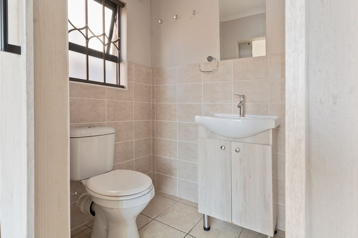 A clean, compact bathroom featuring a modern vanity with basin, toilet, and neutral wall tiling with a security-grilled window.