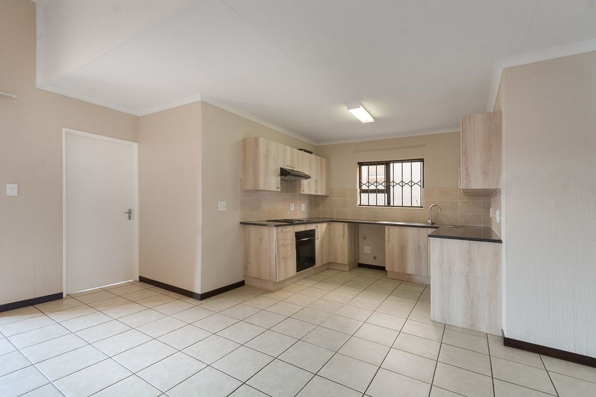 A clean, functional kitchen featuring light wood-finish cabinetry, dark countertops, built-in oven and hob, and tiled flooring throughout.
