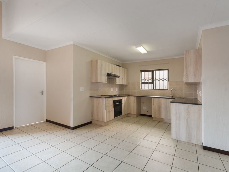 A clean, functional kitchen featuring light wood-finish cabinetry, dark countertops, built-in oven and hob, and tiled flooring throughout.
