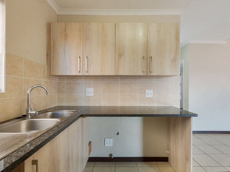 A functional kitchen area featuring light wood-finish cabinetry, granite countertops, and a double stainless steel sink with tiled splashbacks.