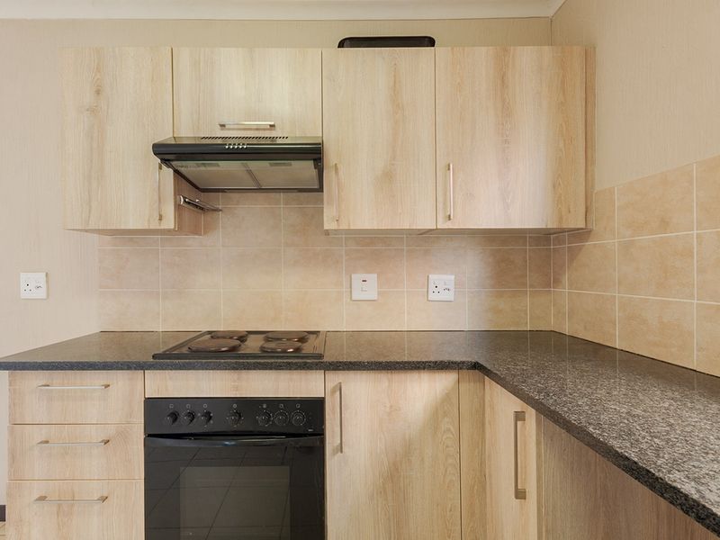 A clean, functional kitchen featuring light wood-finish cabinetry, dark granite countertops, a built-in oven, electric hob, and a tiled splashback.