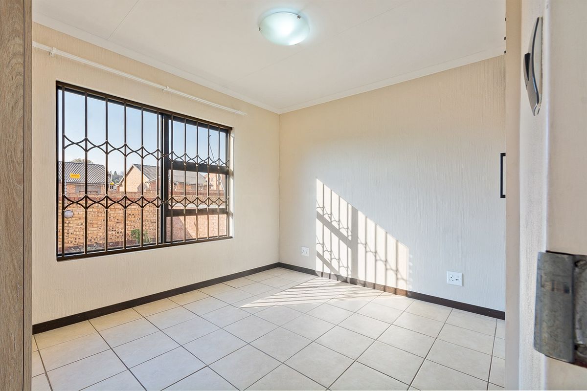 A bright, empty bedroom featuring tiled flooring, neutral walls, and a window fitted with security bars.