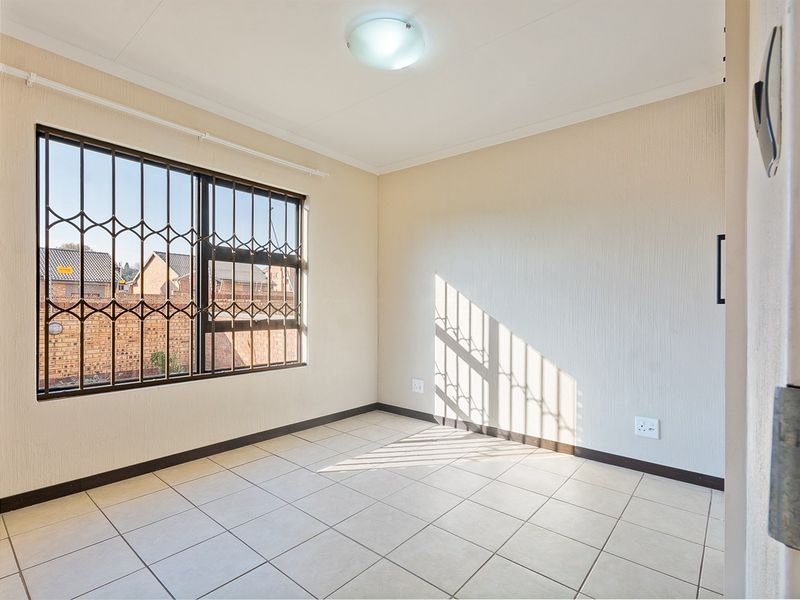 A bright, empty bedroom featuring tiled flooring, neutral walls, and a window fitted with security bars.