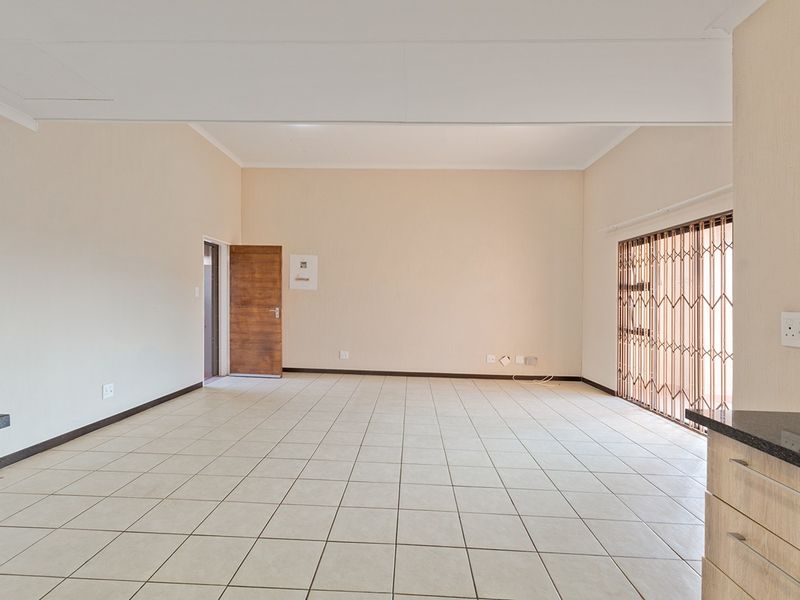 Spacious open-plan living area featuring neutral ceramic floor tiles, built-in kitchen cabinetry with granite countertops, and a secure sliding door entrance.