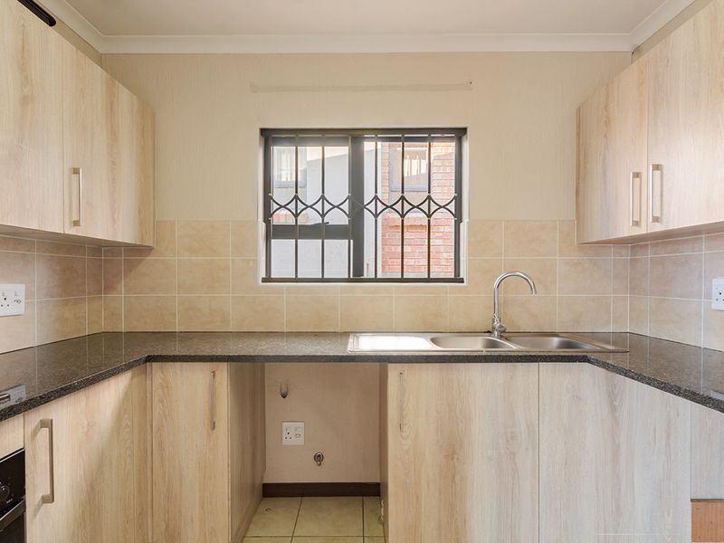 A functional kitchen featuring light wood-finish cabinetry, granite countertops, a double sink, and built-in oven, with space provided for an under-counter appliance.