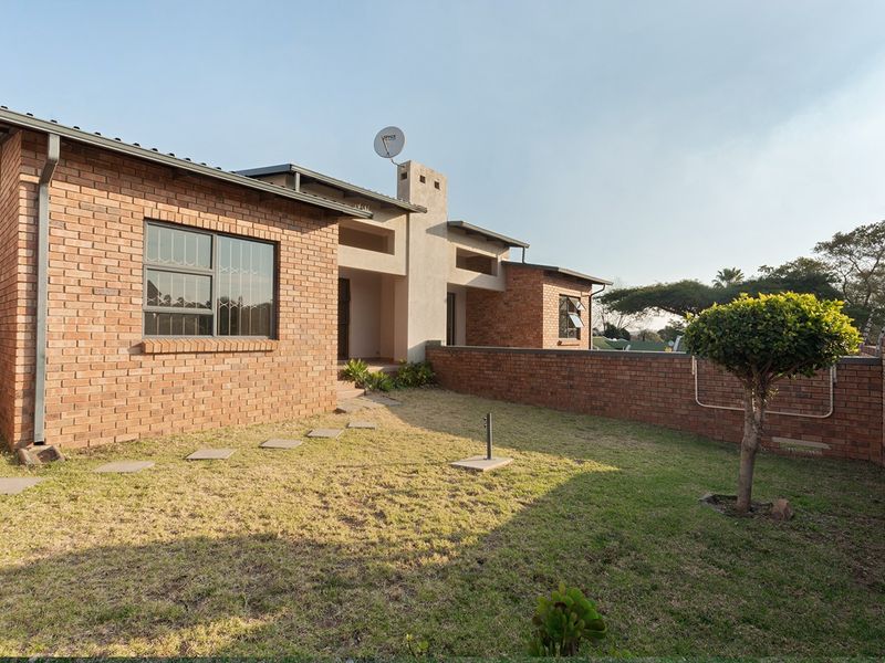 A view of the rear exterior of the townhouse featuring face brick construction, a private garden area, and secure perimeter walling.